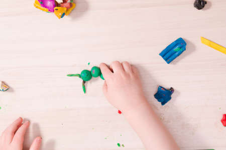 a small child sculpts a caterpillar from green plasticine on a wooden table, the development of fine motor skills of hands than to entertain a child at home, stay at homeの写真素材