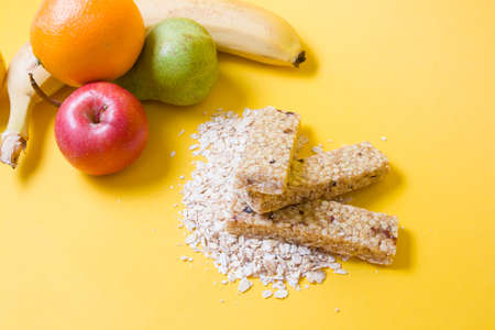 several muesli and fruit bars on a pile of dry oatmeal and various fruits on a yellow background, proper nutrition concept, and healthy snackの写真素材