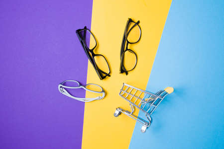 several different glasses and a small shopping cart on a colorful background, top view, buying glasses, a store of glasses and frames for glasses, children's glasses and glasses for adultsの写真素材