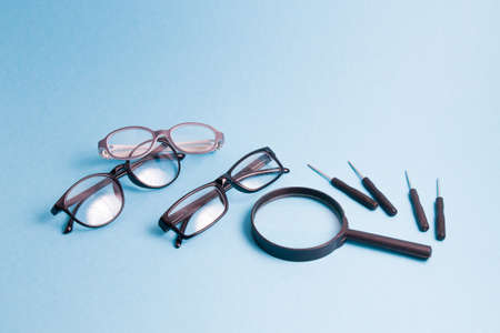a magnifier, several pairs of glasses and small screwdrivers are on a blue background, children's glasses and glasses for adults are being repairedの写真素材