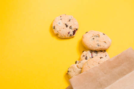 homemade cookies with pieces of chocolate and lingonberries in a paper bag on a yellow background...