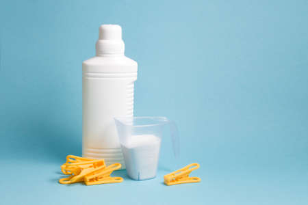 bottle with liquid gel for washing without a label and a measuring cup with washing powder, blue background copy space, washing white linen, a few yellow clothespins on the tableの写真素材