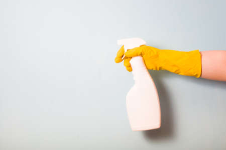 female hand in a yellow rubber glove holds a white spray bottle, spray bottle without a label on a light blue background, copy spaceの写真素材