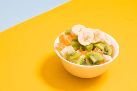 fruit salad in a small white bowl on a yellow backgroundの写真素材