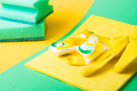 rubber gloves, capsules for dishwashers and sponges on a green and yellow background, places of copy...