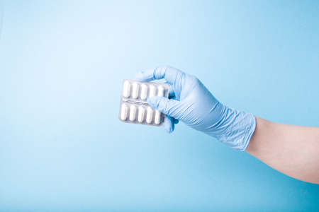 hand in a blue disposable medical glove holds a blister with white capsules blue background copy spaceの写真素材
