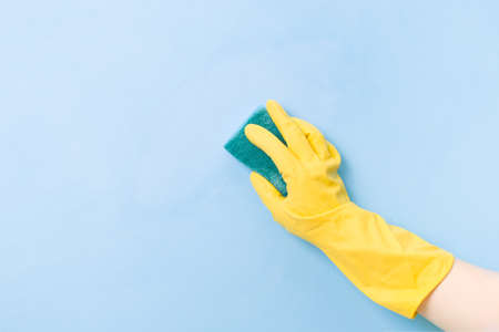 a hand in a yellow rubber glove holds a yellow sponge with a green rough side for cleaning complex dirt, blue background copy space, cleaning concept, home care, spring cleaningの写真素材