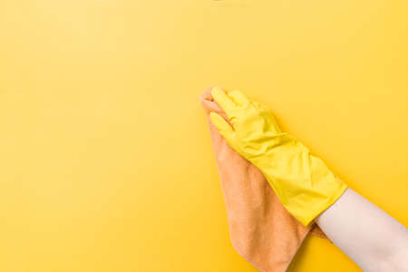 hand in a yellow rubber glove holds an orange rag for washing and cleaning, yellow background copy space, cleaning concept, household chores, wipe the dust and wash the wallsの写真素材