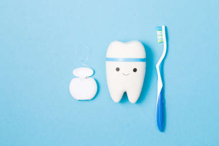 sweets, toothbrush, dental floss and toy tooth on a blue background, tooth model with a smile, protection of the oral cavity from caries concept, pediatric dentistry advertisingの写真素材