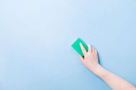 hand without a glove holds a green sponge for washing dishes and cleaning, blue background copy space, cleaning concept, wash painted wallsの写真素材