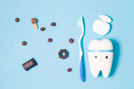 sweets, toothbrush, dental floss and toy tooth on a blue background, tooth model with a smile, protection of the oral cavity from caries concept, pediatric dentistry advertisingの写真素材
