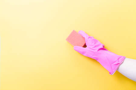 hand in pink rubber glove holds orange sponge for washing dishes and cleaning, yellow background copy space, cleaning conceptの写真素材