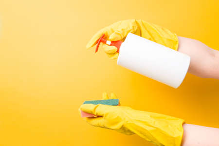female hands in yellow rubber gloves hold a soap dispenser and a sponge for washing dishes and...