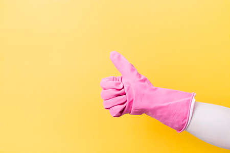 hand in a pink rubber glove for cleaning with a raised thumb up on a yellow background copy space,...