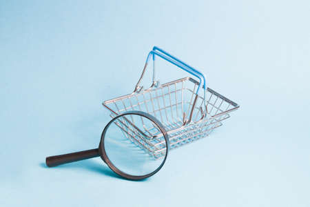 magnifier and small toy shopping basket on a blue background, copy space, shopping conceptの写真素材