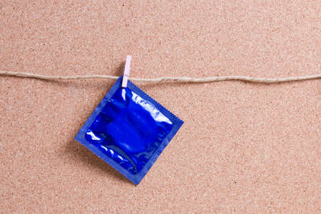 dark blue condom packaging hanging on a small wooden clothespin on a paper thread against the...