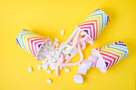 different types of marshmallows dropped from festive paper cups with geometric pattern on yellow...
