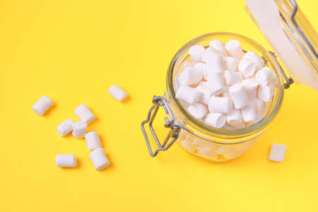 small white marshmallows in a jar on a yellow background copy space, an ingredient for making a Christmas drink and decorating cakesの写真素材