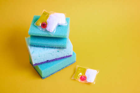gel capsules for dishwashers and sponges on a green and yellow background of the places of the copy...