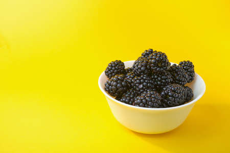 Dewberry. Blackberries in a wooden bowl on a light table. Fresh blackberries in a bowl close-up. Space for textの写真素材