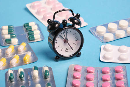 black small alarm clock and packaging of pills on blue background, copy space, medication taking by time, medication taking reminder conceptの写真素材