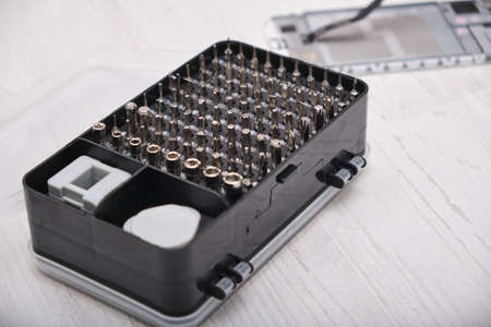 a close-up of a set of screwdriver bits in a black box, gloves, a broken smartphone and a set of...