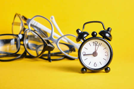 alarm clock and several different eye glasses on yellow background, glasses for children and adults, copy place, glasses purchase conceptの写真素材