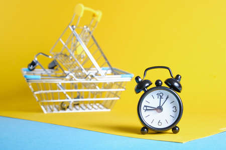 alarm clock and miniature shopping basket on yellow backgroundの写真素材