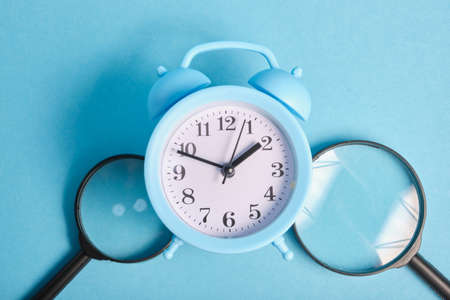 magnifiers and light blue alarm clock on a blue background