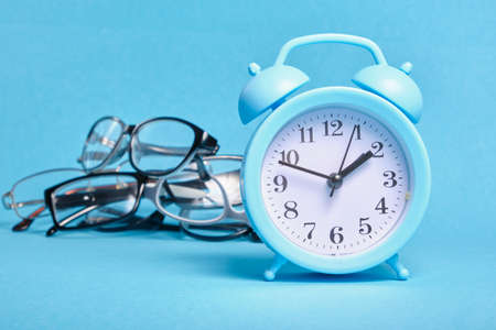 alarm clock and several different eye glasses on a blue background, glasses for children and adults, copy place, buy glasses conceptの写真素材