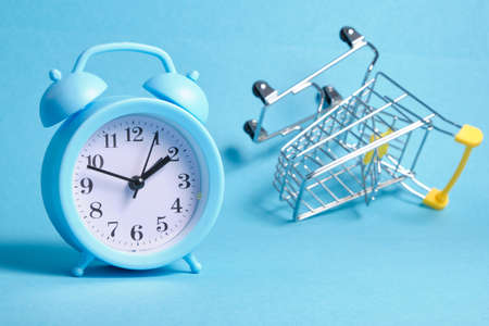 alarm clock and miniature shopping trolley on blue background copy spaceの写真素材