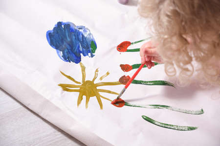 a small child draws with paints on a large sheet of paper, a child draws flowers, sun and sky