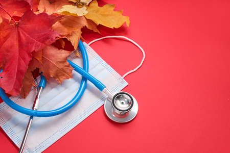 disposable protective medical mask and stethoscope and autumn maple leaves on a red backgroundの写真素材