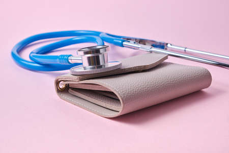 Stethoscope on an old wallet on pink background.