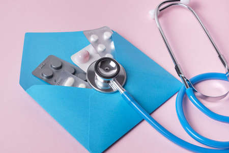 pills in a blue envelope and a medical stethoscope on a pink backgroundの写真素材