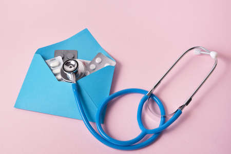 pills in a blue envelope and a medical stethoscope on a pink backgroundの写真素材