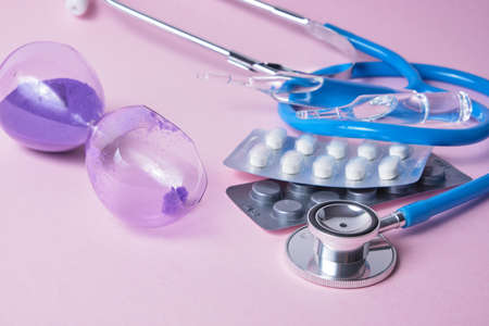 stethoscope, broken hourglass and medicine on a pink background copy spaceの写真素材