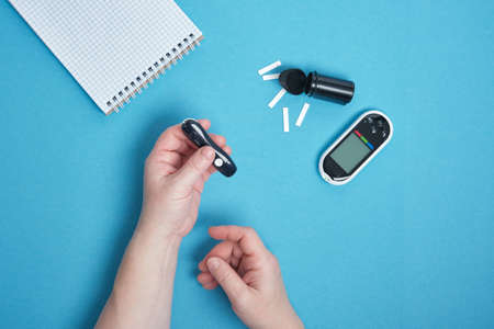 woman hand using a lancet on her finger to check blood sugar using a glucose meter ,, diabetes, glycemia, healthcare concept. blue background copy space top viewの写真素材