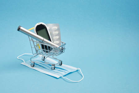 Diabetes concept. Diabetic supplies in shop trolley, pills, glucose meter, insulin syringe pen on blue backgroundの写真素材
