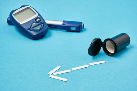 glucose meter and syringe pen for insulin injections on a blue background, test strips for measuring...
