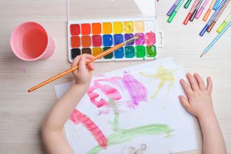 the child draws with a brush on paper, drawing with watercolors at the table, creativity for children, development of imagination in childrenの写真素材