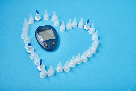 insulin needles in the form of a heart on a blue background and a blood glucose meter in the centerの写真素材