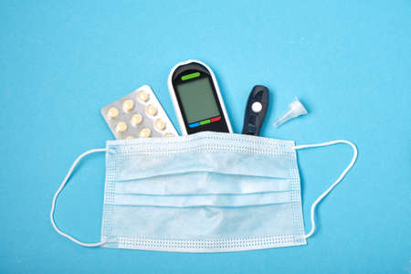 black blood glucose meter, lancet, blister pills and face mask on a blue background,の写真素材