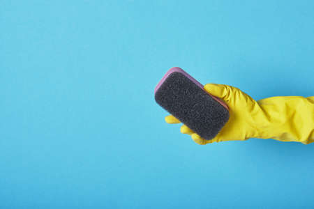 Hand in yellow glove with sponge on blue background copy spaceの写真素材