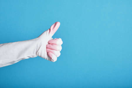 A hand in a yellow white glove shows a thumb up on a bright blue background. copy spaceの写真素材