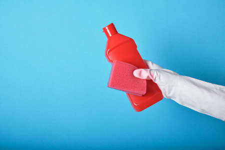Lifestyle home keeping concept. hand in rubber glove holds red bottle with washing gel. Detergent...