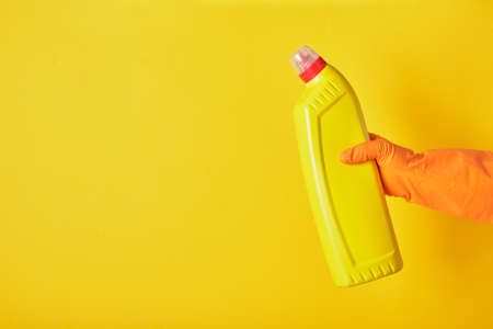 Lifestyle home keeping concept. hand in rubber glove holds yellow bottle with washing gel. for...