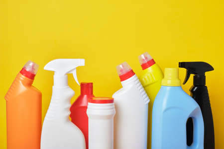 Colored plastic detergent bottles on yellow background copy space