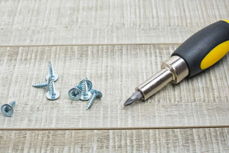 screws for metal and a screwdriver with replaceable nozzles on a wooden background copy space