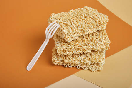 white disposable plastic fork and three block of dry instant noodles on beige and brown background copy spaceの写真素材